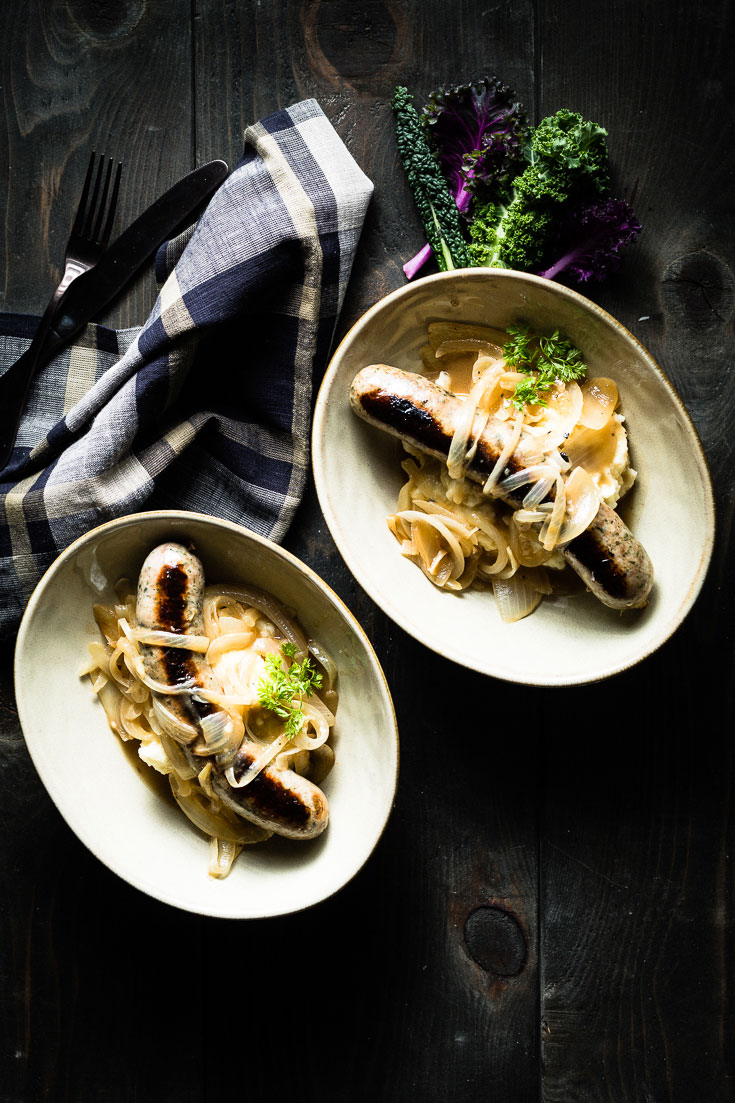 Bangers and Mash in bowls on dark wood table
