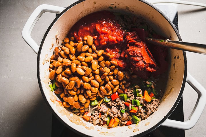 adding beans and tomatoes to chili