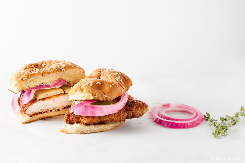 Crispy Pork Sandwich sliced in half with Pickled Onions