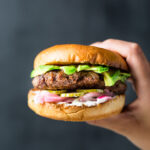 Holding Lamb Burger with Pickled Veggies and Yogurt-Mint Sauce vertical
