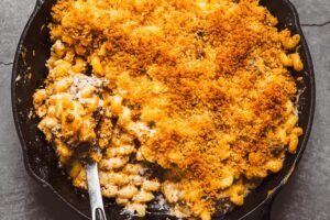 Extreme close-up of creamy smoked lamb mac and cheese in a black cast iron skillet, topped with a crispy, golden breadcrumb crust.