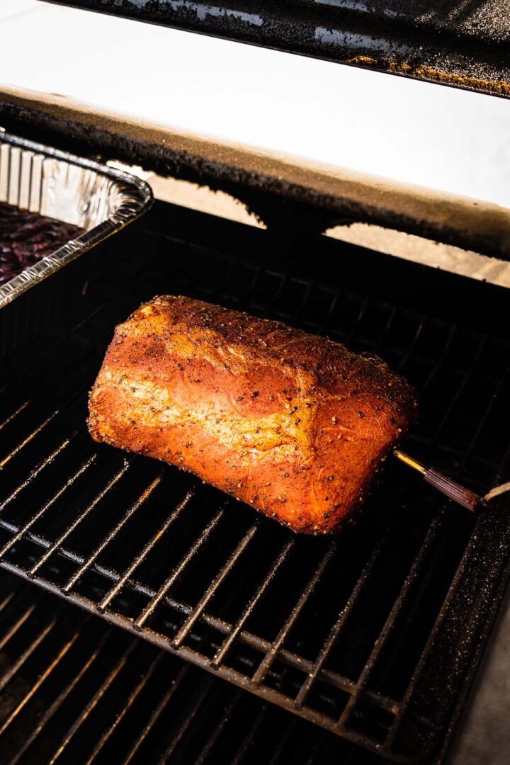 Seasoned pork loin in a smoker with a probe thermometer inserted.