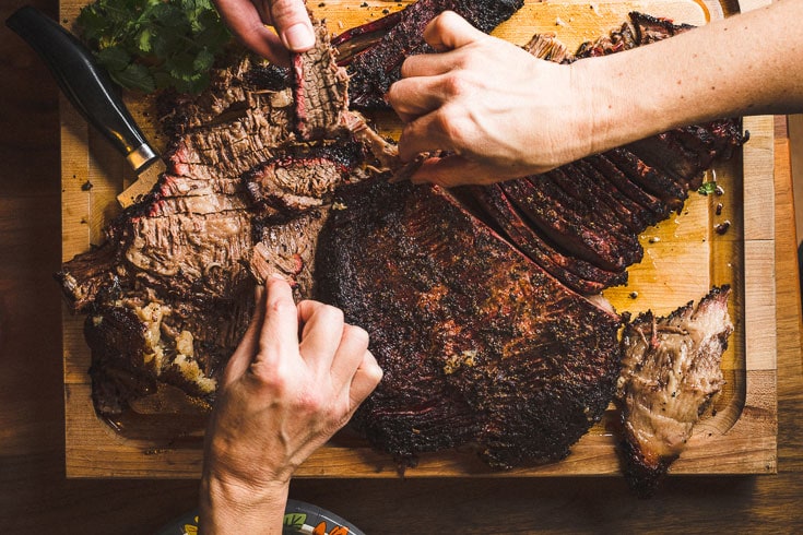 Smoked beef Brisket Sliced on a Cutting board overhead with hands reaching in