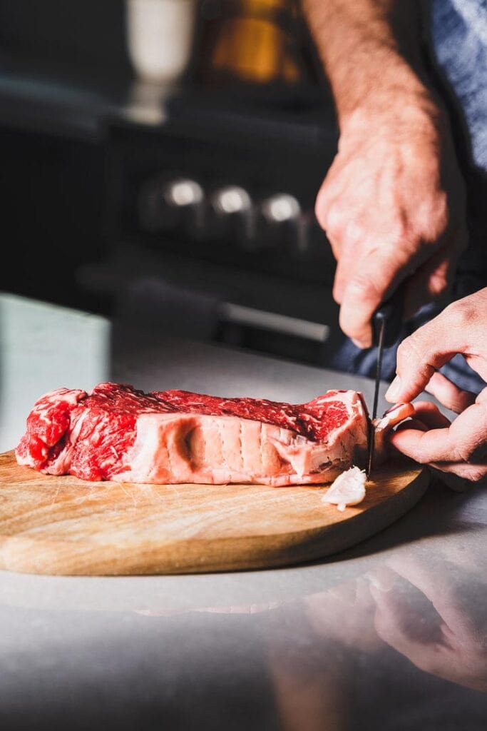 trimming a New York Strip Steak on cutting board
